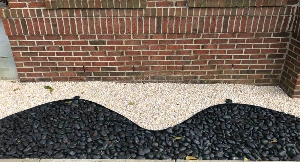 Black river stone bed with curved edging against a brick wall
